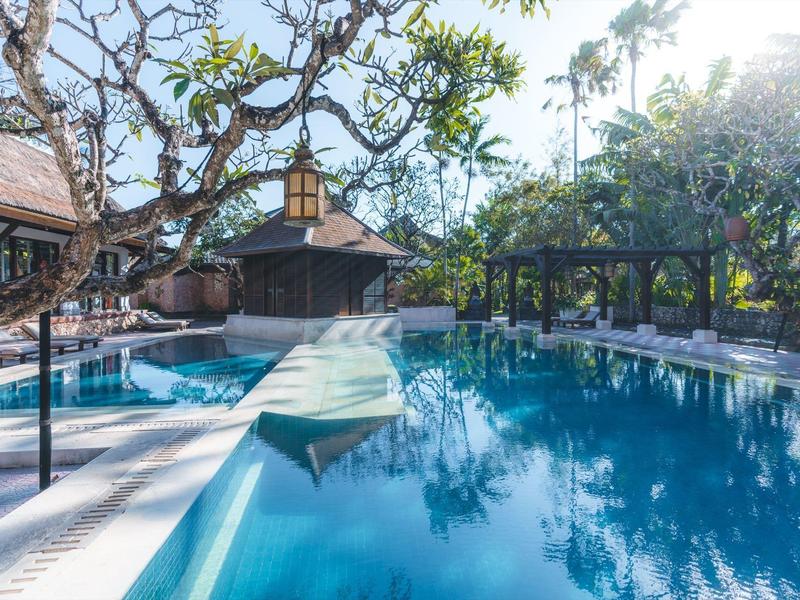 Een groot, rustig zwembad omgeven door bomen en traditionele gebouwen onder een heldere hemel.