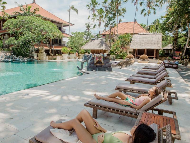 Ontspannen persoon liggend op een ligstoel bij een zwembad in een tropisch resort.