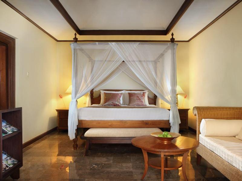 Ruime hotelkamer met hemelbed, bank, houten meubels en warm licht.