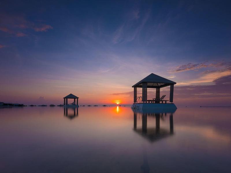 Zonsondergang boven kalm water met twee decoratieve paviljoens in het water.