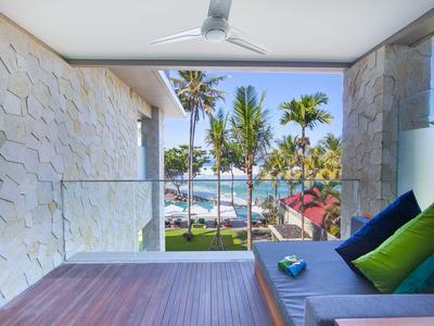 Moderner Balkon mit Holzfußboden, grauem Sofa, bunten Kissen und Blick auf Palmen und Meer.