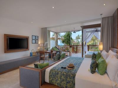 Helles Schlafzimmer mit großem Bett, grün gemusterten Kissen, Balkon und Fernseher an der Wand.