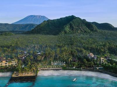 Küste mit klarem türkisfarbenem Wasser, grünen Hügeln und einem hohen Berg im Hintergrund.