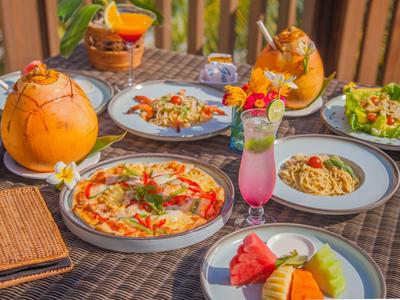 Bunt gedeckter Tisch mit Pizza, Pasta, Salaten, Früchten und tropischen Cocktails auf Terrasse.