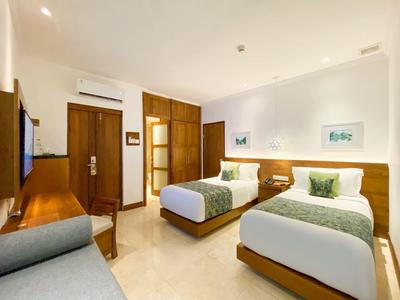 Helles Hotelzimmer mit zwei Einzelbetten, Holzmöbeln, Sofa und Klimaanlage an der Wand.