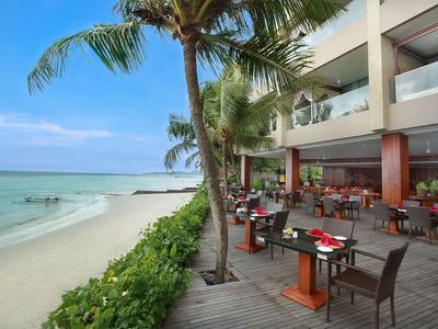 Area pranzo esterna di un ristorante sulla spiaggia con vista sull'oceano e palme.