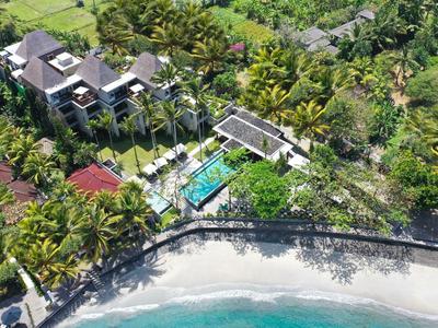 Villa di lusso con piscina circondata da vegetazione tropicale, adiacente a una spiaggia sabbiosa e al mare.
