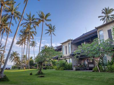 Großes Haus mit Veranda, umgeben von hohen Palmen und grünem Rasen unter blauem Himmel.