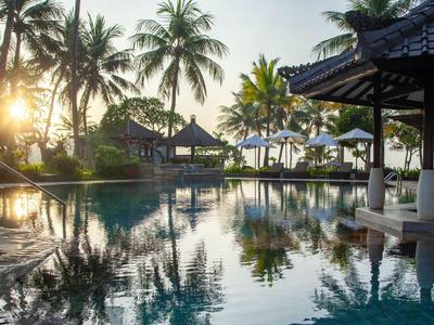 Ein ruhiger Pool mit Palmen und Sonnenschirmen bei Sonnenuntergang am Strand.