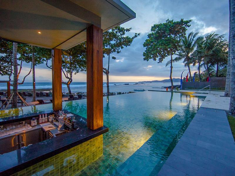 Infinity-Pool mit Bar, umgeben von Bäumen, Blick auf den Ozean bei Abenddämmerung.