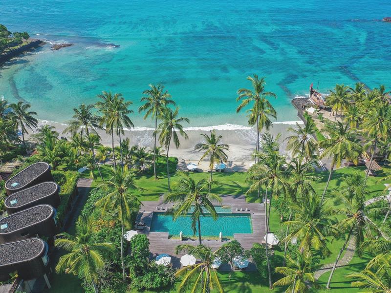 Tropischer Strand mit türkisfarbenem Meer, Palmen, Pool und grüner Vegetation.