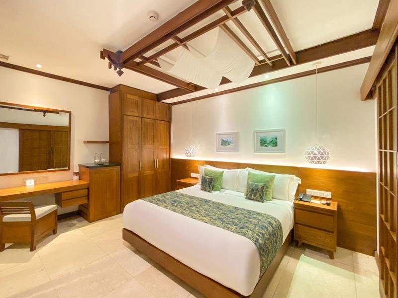 Helles Schlafzimmer mit Holzmöbeln, Doppelbett, Spiegel, Tisch und dekorativen Kissen.