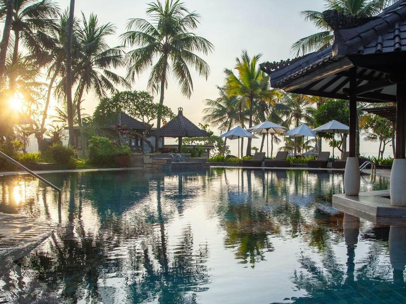 Ein ruhiger Pool mit Palmen und Sonnenschirmen bei Sonnenuntergang am Strand.