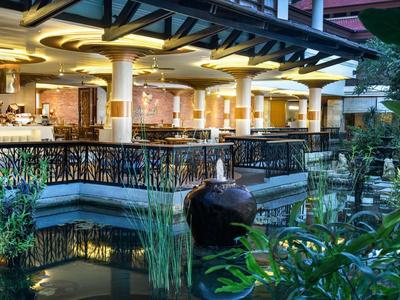 Hotelterras met bar en decoratief waterornament in tropische omgeving bij schemering.