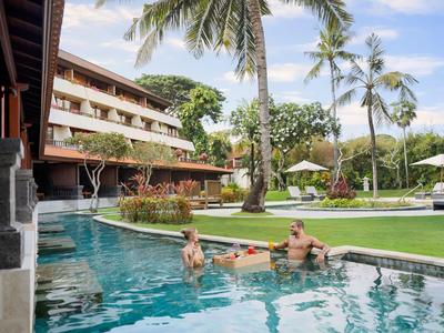 Zwembadgebied van een resort met ligstoelen, parasols en palmbomen in de tuin.