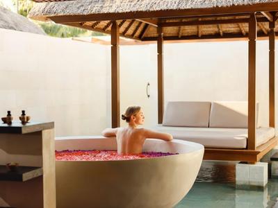 Persoon ontspant in een badkuip met rozenblaadjes onder een buitenpaviljoen