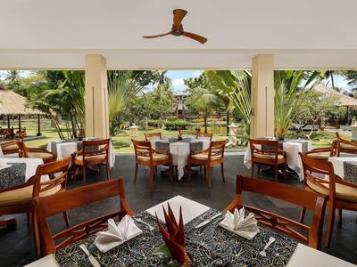 Open restaurantgedeelte met gedekte tafels en uitzicht op tropische tuin.