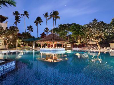 Evening pool with palm trees and illuminated pavilion at a tropical resort.