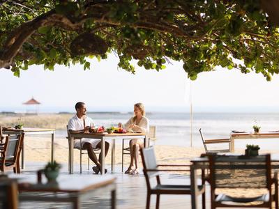 Couple sitting outdoors under shady trees with a sea view, drinking beverages.