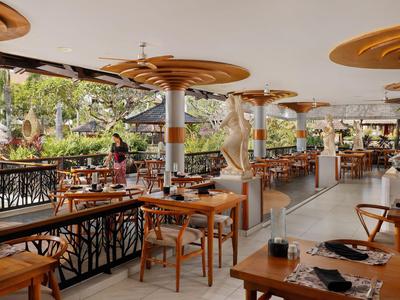 Modern restaurant with wooden tables and open windows overlooking tropical garden.