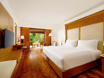 Elegant hotelkamer met groot bed, houten vloer en zithoek met uitzicht op de natuur.