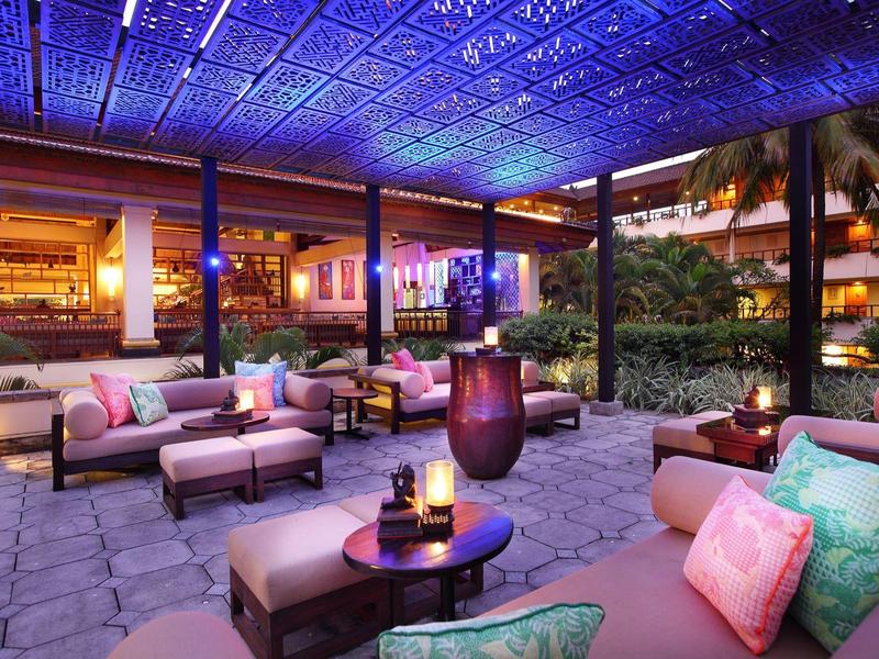 Gezellige buitenlounge met banken en kussens in hotelomgeving bij nacht met sfeerverlichting.