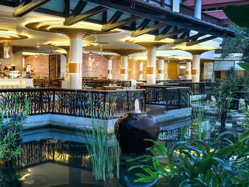 Hotelterras met bar en decoratief waterornament in tropische omgeving bij schemering.