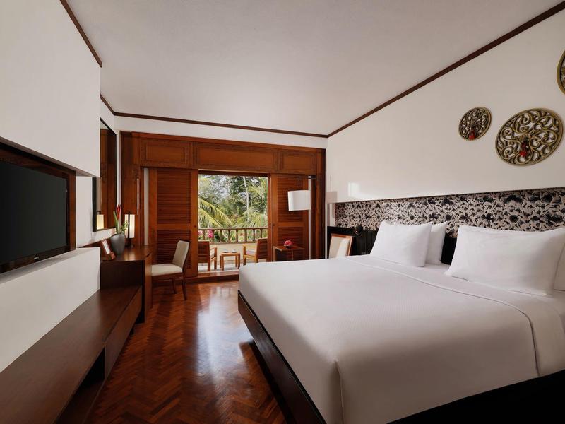 Modern hotelkamer met tweepersoonsbed, bureau en balkon met uitzicht op groen landschap.