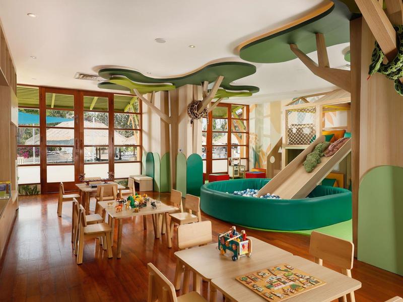 Speelruimte voor kinderen in hotel met tafels, stoelen en speeltoestellen in boomstijl.