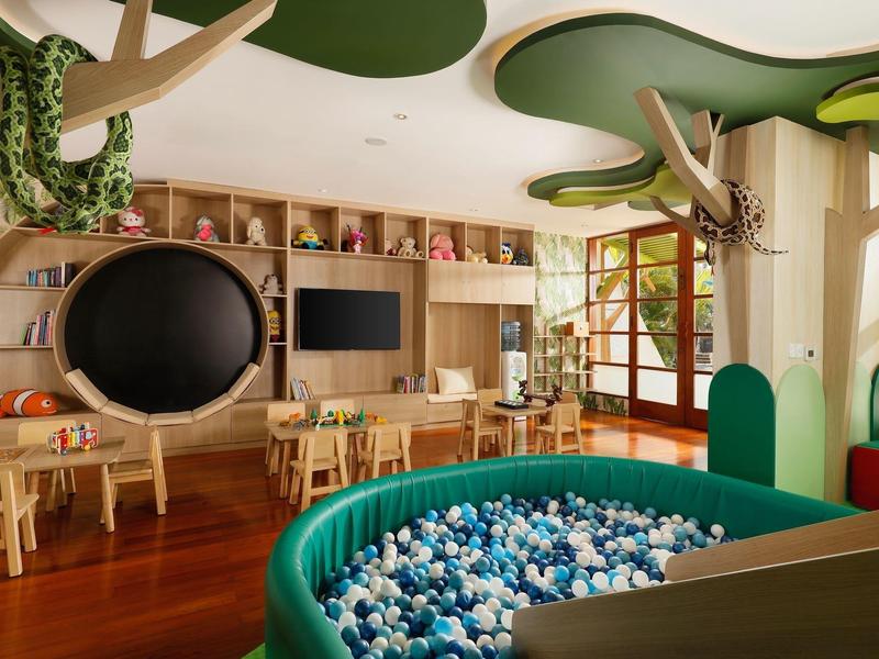 Speelkamer voor kinderen met ballenbak, houten speelgoed en uniek boomstamontwerp aan het plafond.