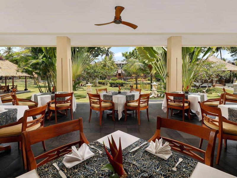 Open restaurantgedeelte met gedekte tafels en uitzicht op tropische tuin.