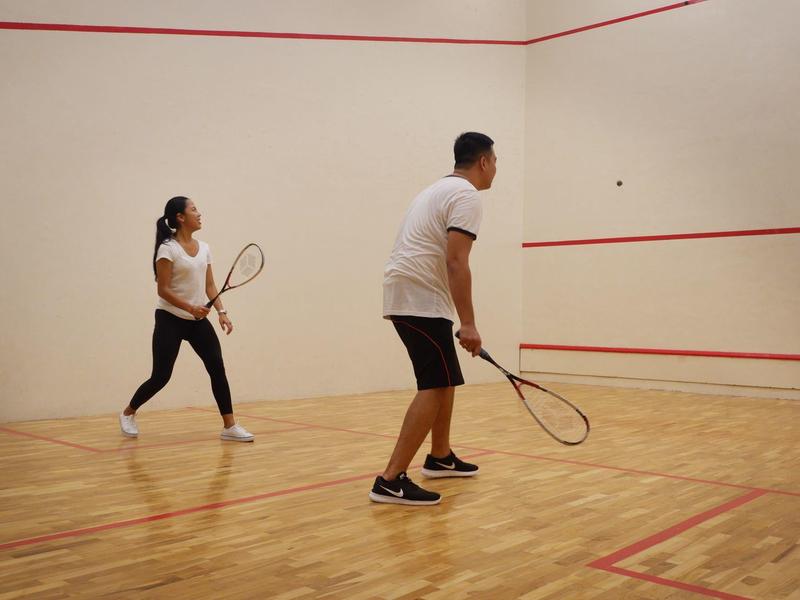 Twee mensen spelen squash in een binnensquashbaan met houten vloer.