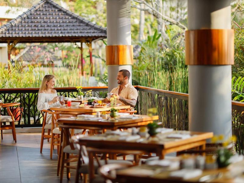 Koppel zit op open veranda en geniet van een maaltijd met natuurzicht.