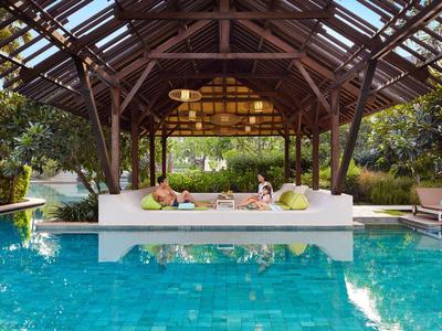 Poolbereich mit überdachtem Sitzbereich und entspannenden Gästen an einem sonnigen Tag.