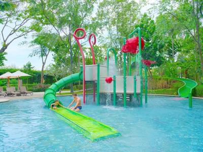 Kind spielt im erfrischenden Schwimmbecken mit Wasserrutschen und Spielgeräten in grüner Natur.