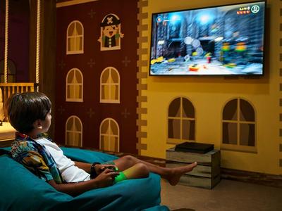 Kind sitzt auf einem Sessel und spielt Videospiele in einem gemütlichen Raum mit Fernseher.