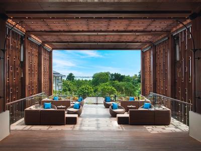 Offener Lounge-Bereich mit Sitzmöbeln und Blick auf Pool und Garten bei klarem Himmel.