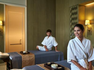 Zwei Personen in Bademänteln in einem ruhigen Wellness- oder Massageraum mit warmem Licht.