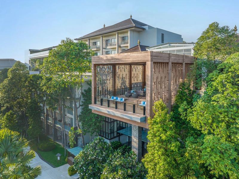 Hotel mit Balkon, umgeben von grünen Bäumen unter klarem Himmel.