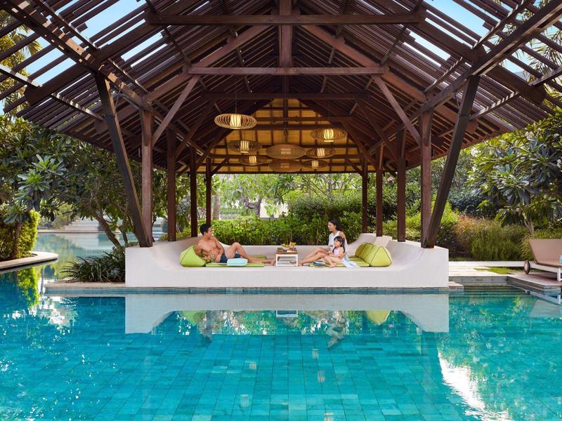 Poolbereich mit überdachtem Sitzbereich und entspannenden Gästen an einem sonnigen Tag.