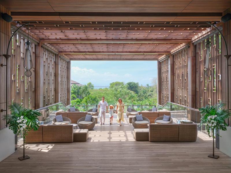 Offener Lounge-Bereich mit Sofas, Pflanzen und Blick auf Garten und Meer.