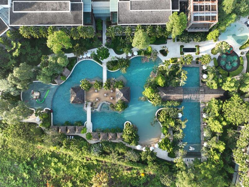 Luftaufnahme eines großen Pools mit Insel, Brücken und viel Grün rundum.