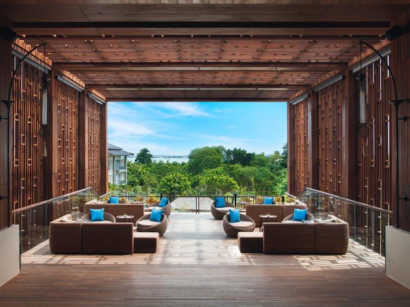 Offener Lounge-Bereich mit Sitzmöbeln und Blick auf Pool und Garten bei klarem Himmel.