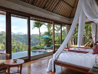Luxurious bedroom with canopy bed overlooking tropical landscape and pool through large glass doors.