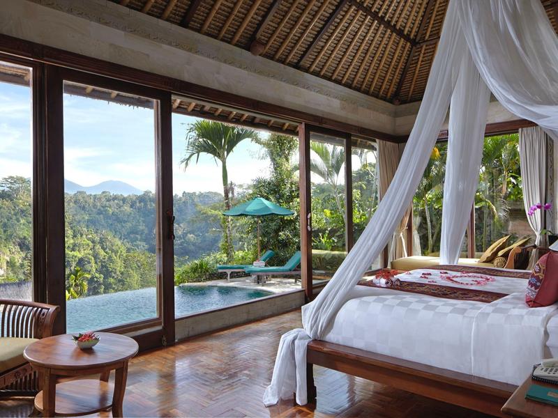 Luxurious bedroom with canopy bed overlooking tropical landscape and pool through large glass doors.