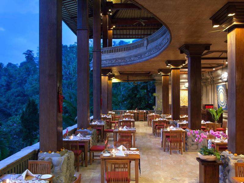 Open-air restaurant with wooden decor and lush green forest view at dusk.