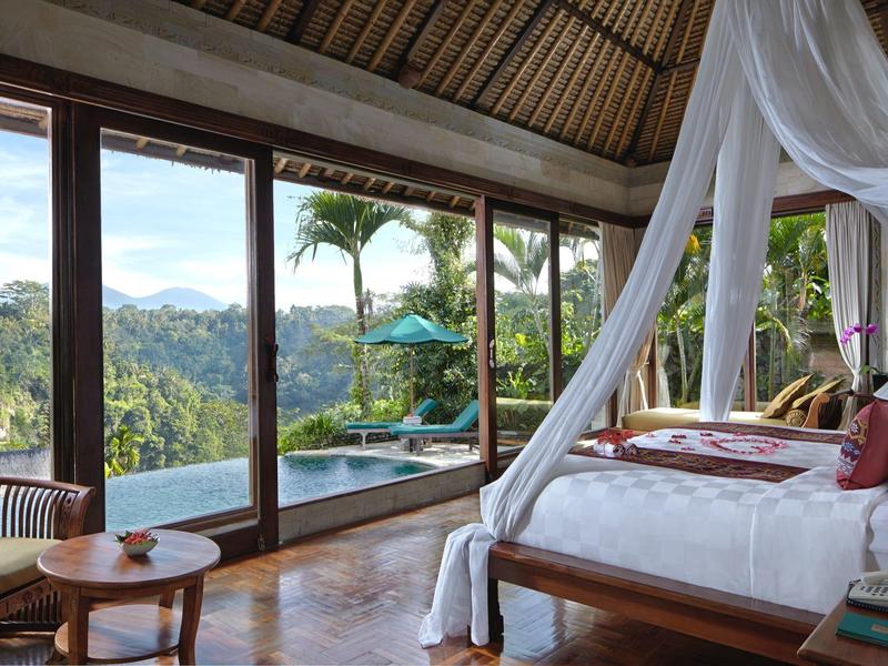 Luxurious bedroom with canopy bed and view of pool and tropical landscape.