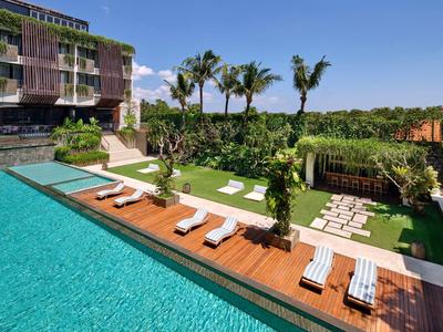 Nowoczesny basen na zewnątrz z leżakami i palmami obok budynku hotelowego.