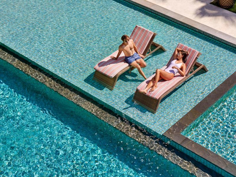 Dwie kobiety wypoczywają na leżakach przy basenie hotelowym.