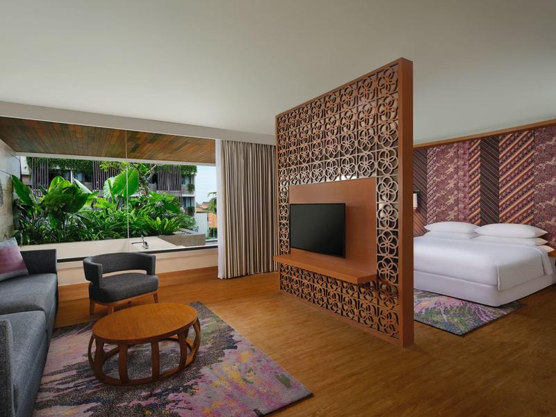 Nowoczesny pokój hotelowy z otwartą częścią dzienną i sypialną oraz widokiem na ogród.